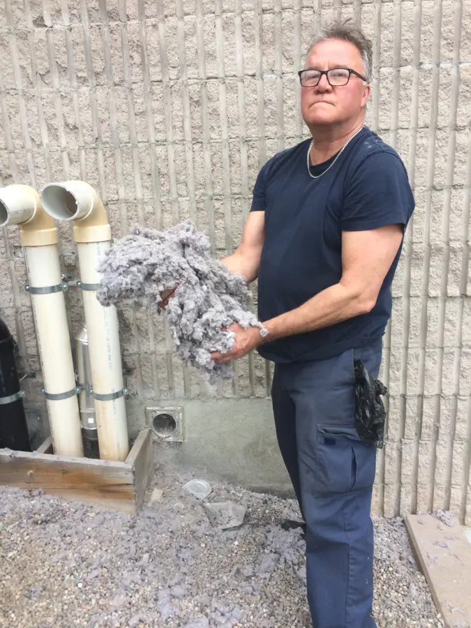Technician holding a large handful of lint pulled from a dryer vent, standing beside the vent piping