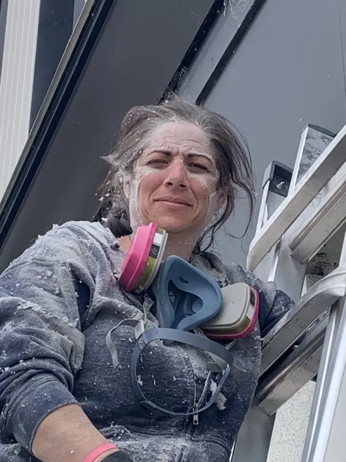 Technician dusted with insulation beside a ladder at the end of a vent-clearing job